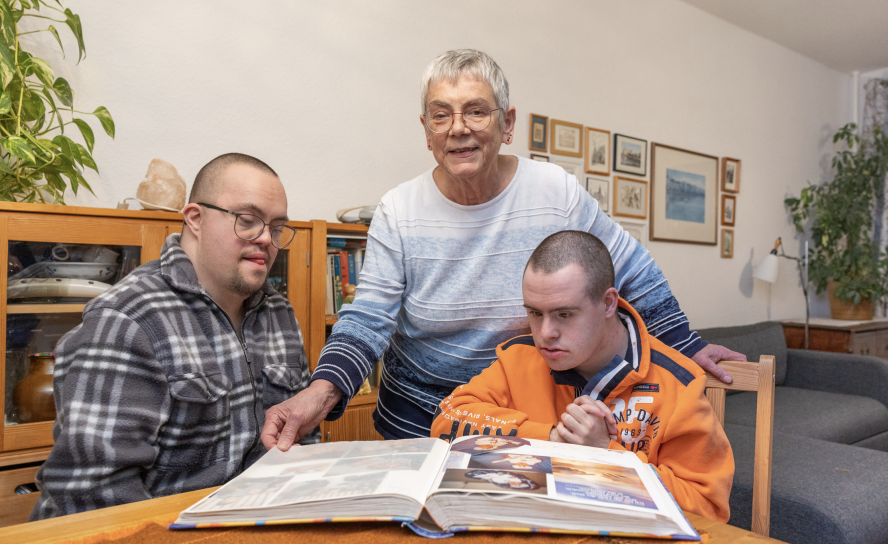 Fotos voller Lebensfreude – auch mit Down-Syndrom: Josef (l.), Dorothea und Jakob Strunze blättern im Fotoalbum, das die beiden jungen Männer in Kindheitstagen zeigt.Foto: Uwe Winkler