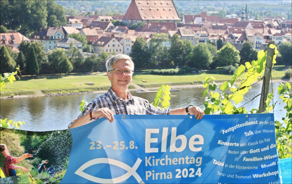 Andreas Steffens, Projektleiter Elbekirchentag im Kirchenbezirk Pirna, mit Werbebanner für den 12. Elbekirchentag – hinter ihm die Elbe, die historische Altstadt mit Stadtkirche St. Marien. © Daniel Förster